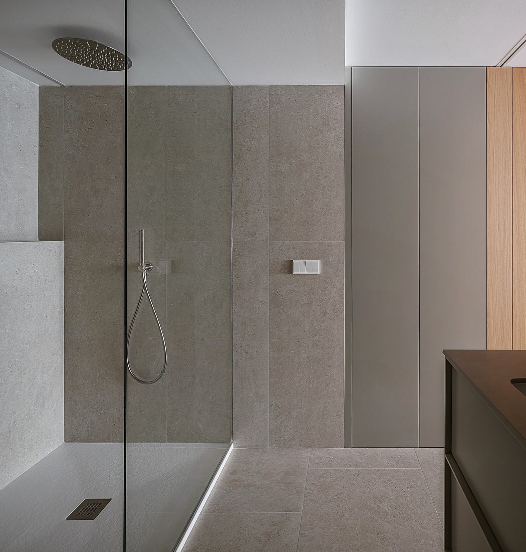 A modern shower enclosure with large gray tiles, a rainfall showerhead, and minimal design.
