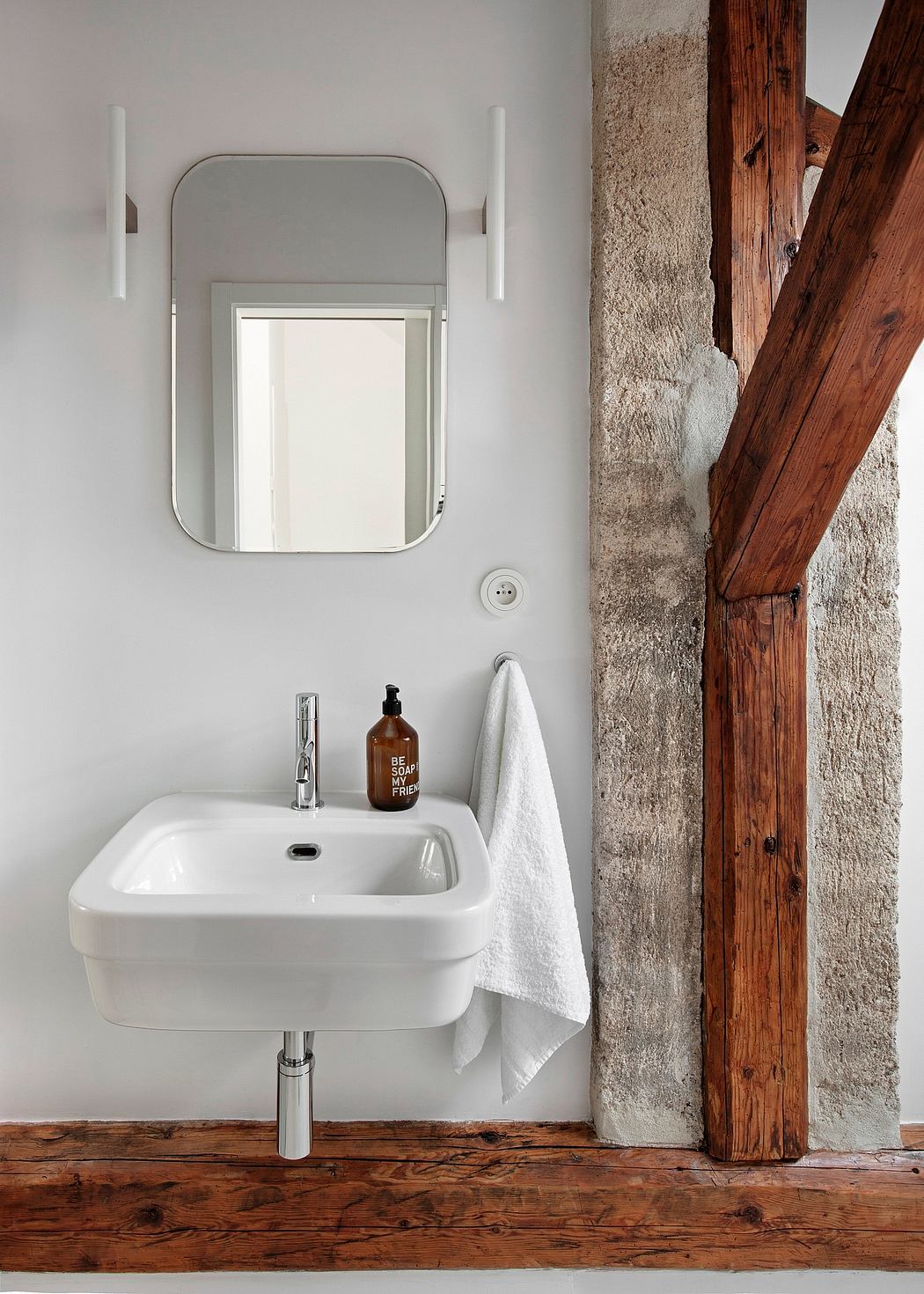 A modern bathroom with an oval white sink, wooden beams, and a frameless mirror.