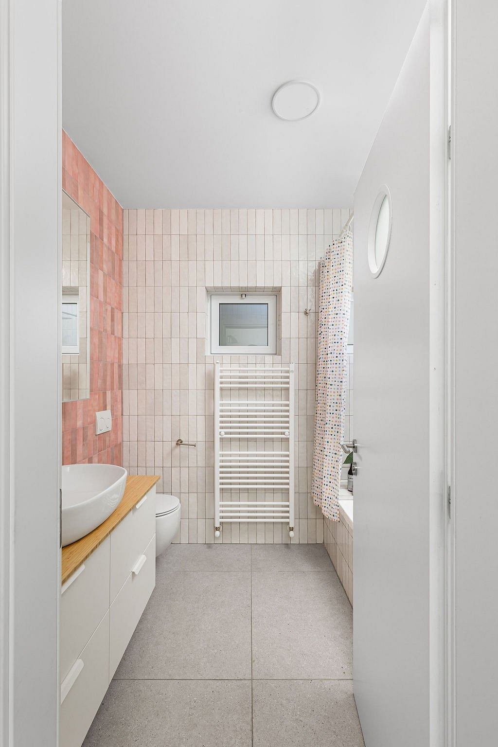 A modern bathroom with pink and white tile, a vanity, and a towel warmer.