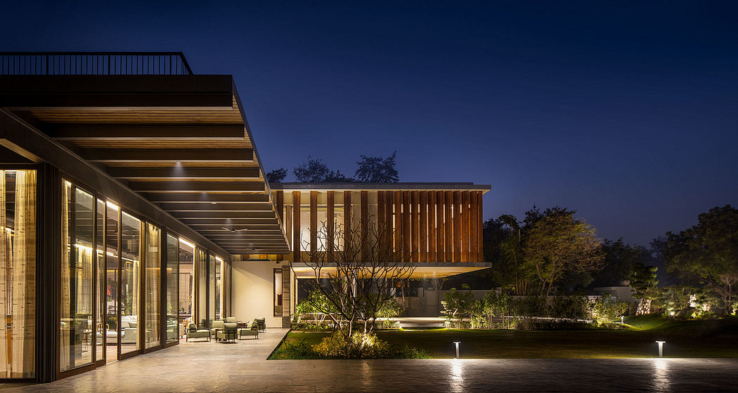 Modern architectural building with wooden elements, glass walls, and illuminated garden at night.