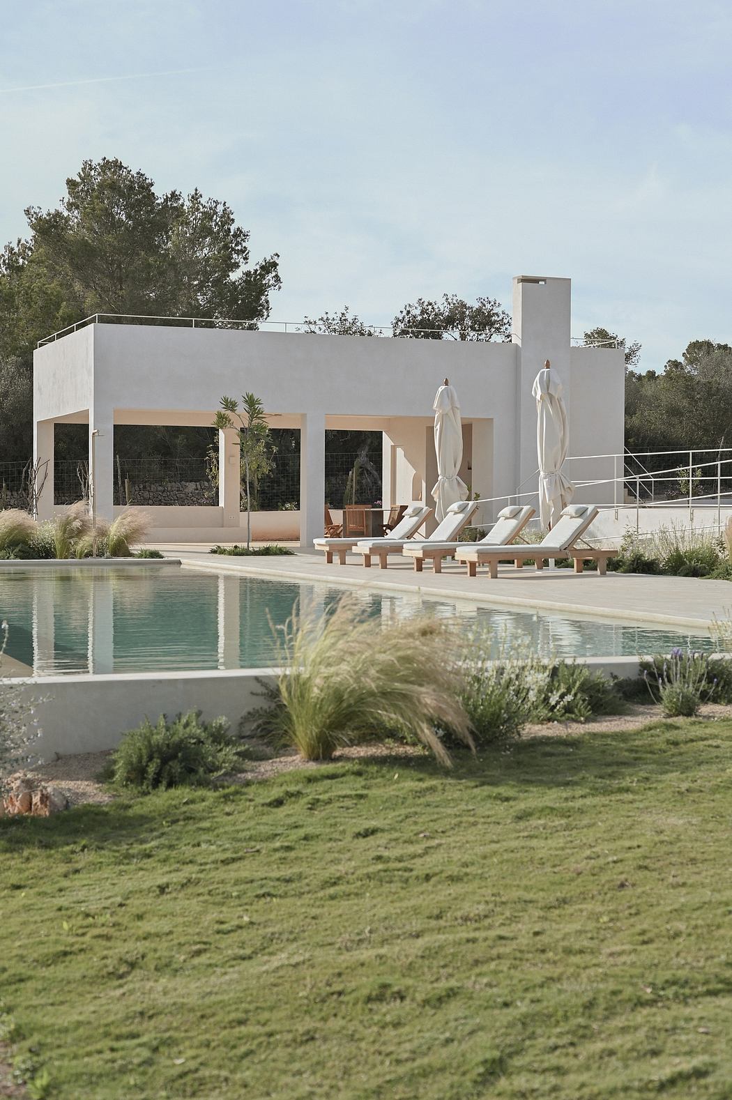 A modern, minimalist building with a sleek, rectangular design and a pool in the foreground. Lush greenery surrounds the property.