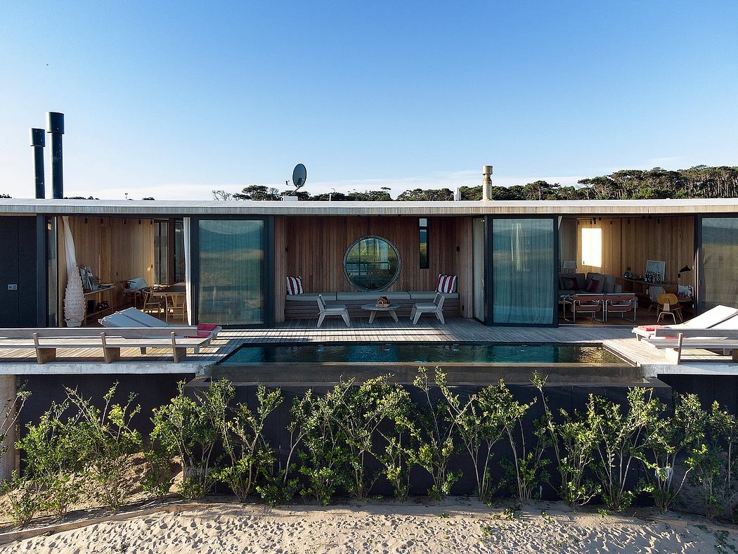 Modern beachfront property with glass walls, wooden deck, and landscaped garden.