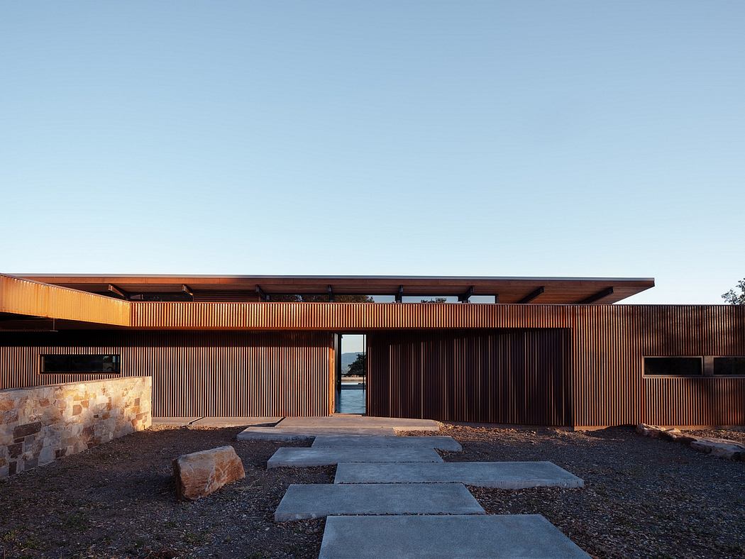 A modern wood-clad building with stone accents and a minimalist concrete pathway.