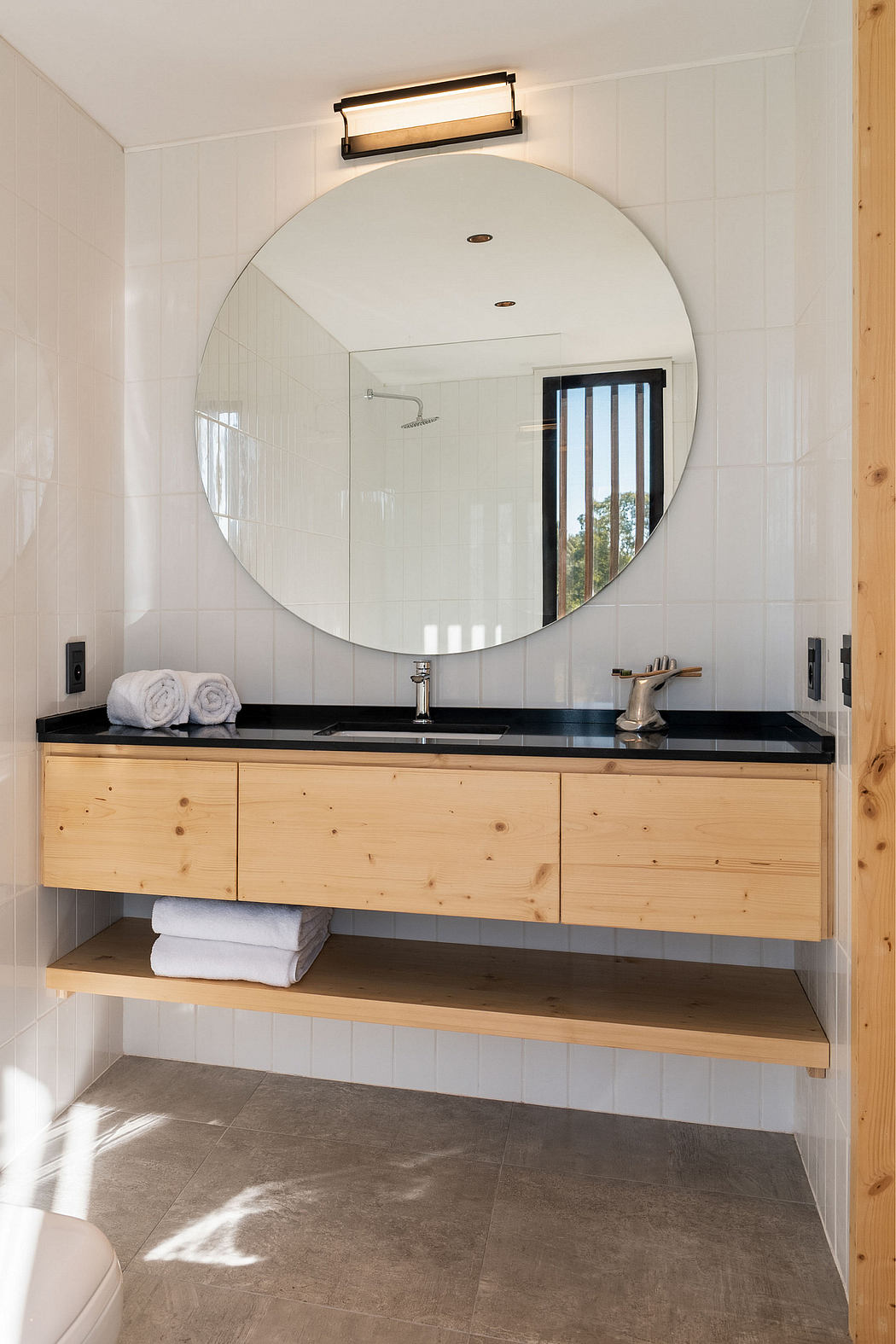 Spacious bathroom with large circular mirror, wooden vanity, and tile flooring.