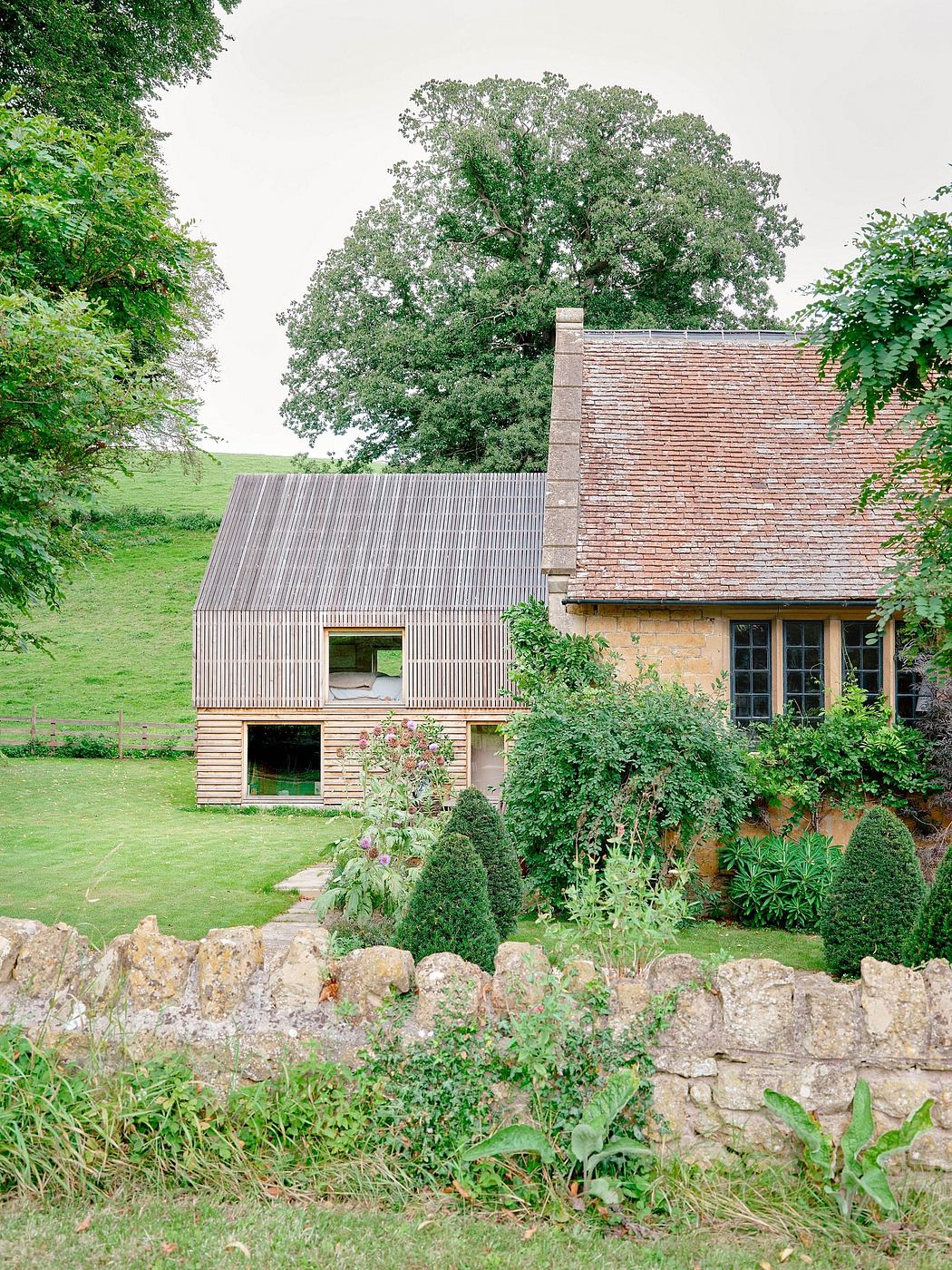 A charming rural home with a mix of brick, wood, and stone, surrounded by lush greenery.