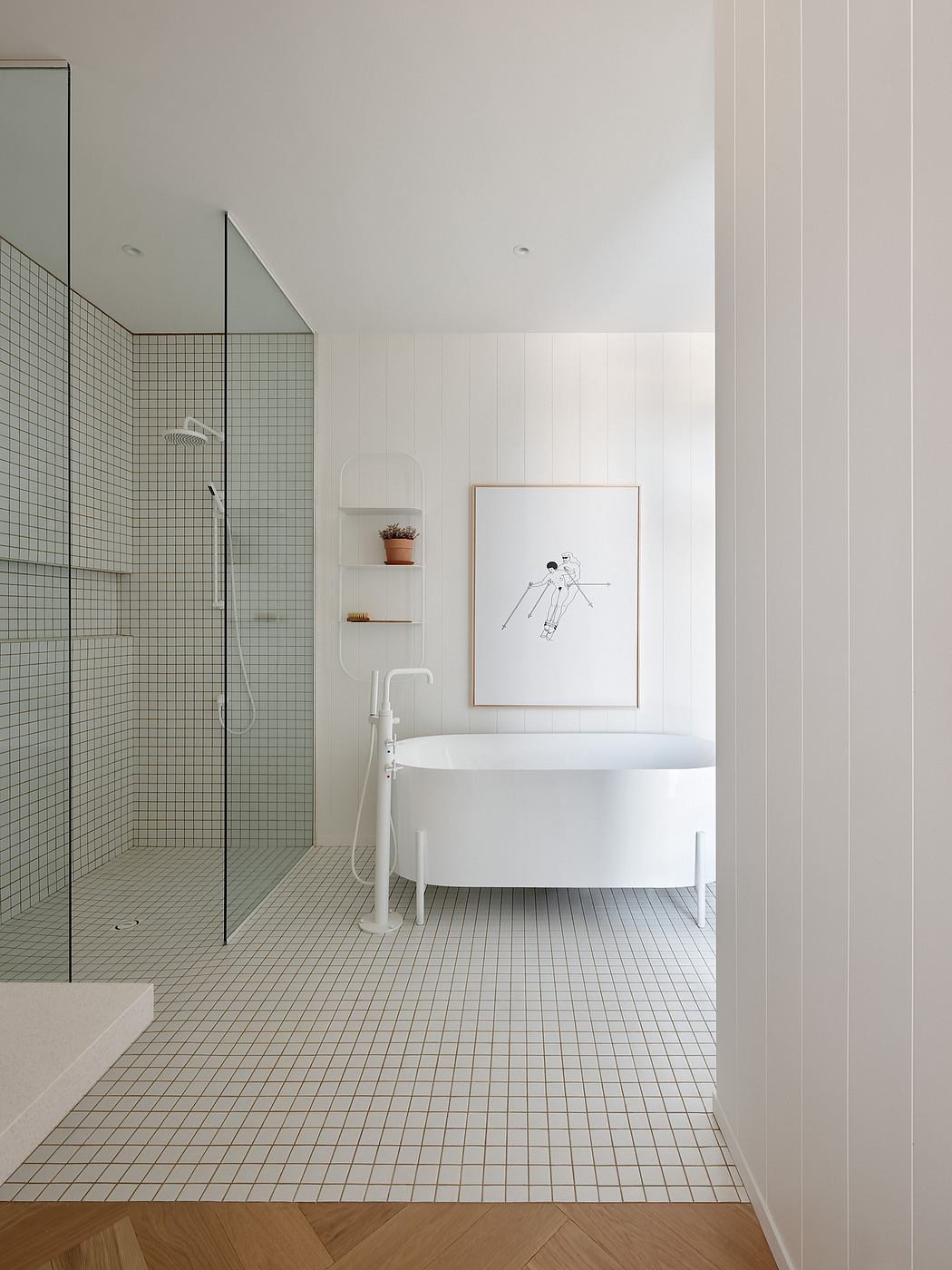 Clean, minimalist bathroom with white tiles, freestanding bathtub, and framed artwork.