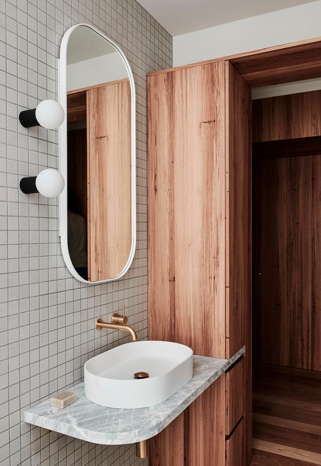 A modern bathroom with a white oval sink, wooden vanity, and arched mirror.