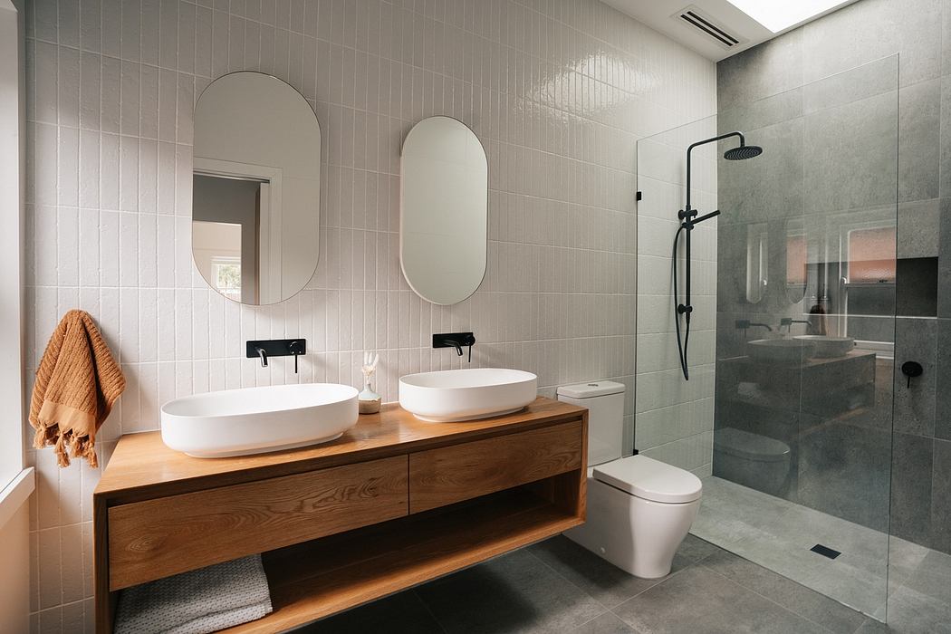Spacious modern bathroom with wooden vanity, oval mirrors, and glass-enclosed shower.