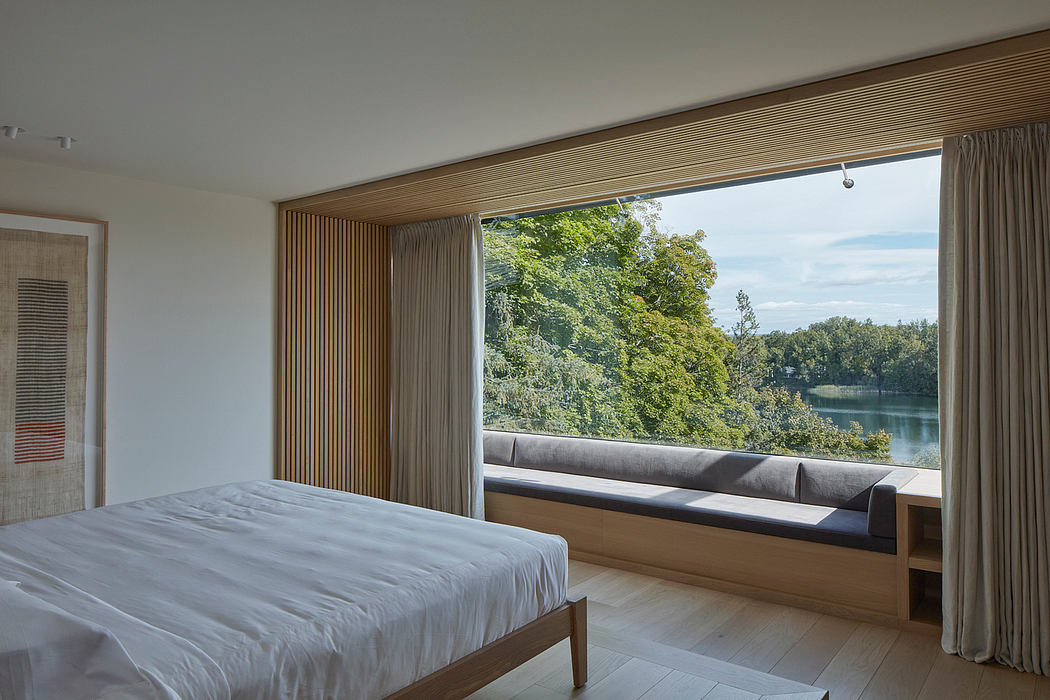Spacious bedroom with floor-to-ceiling windows offering scenic lake view and modern wood paneling.