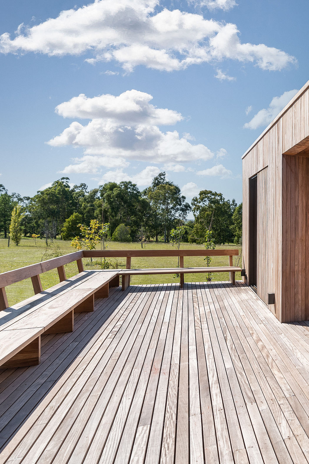 Spacious wooden deck with benches, surrounded by lush greenery and cloudy sky.