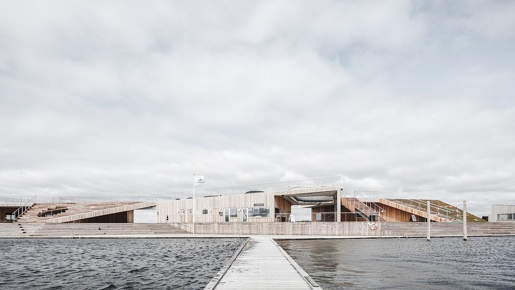 A modern, wooden lakeside structure with a covered walkway and balconies overlooking the water.