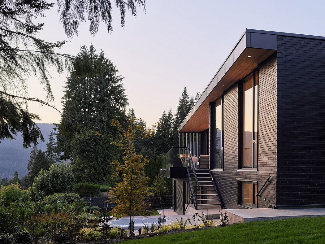 A modern, two-story residence with a black exterior, wooden accents, and a balcony overlooking a forested landscape.