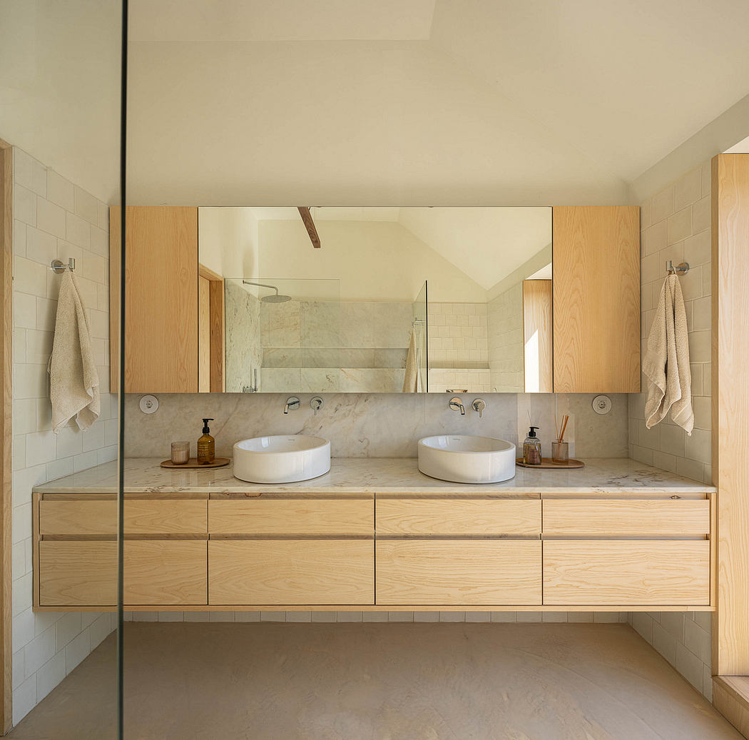 Minimalist bathroom with wood vanity, marble countertop, and vessel sinks under a large mirror.