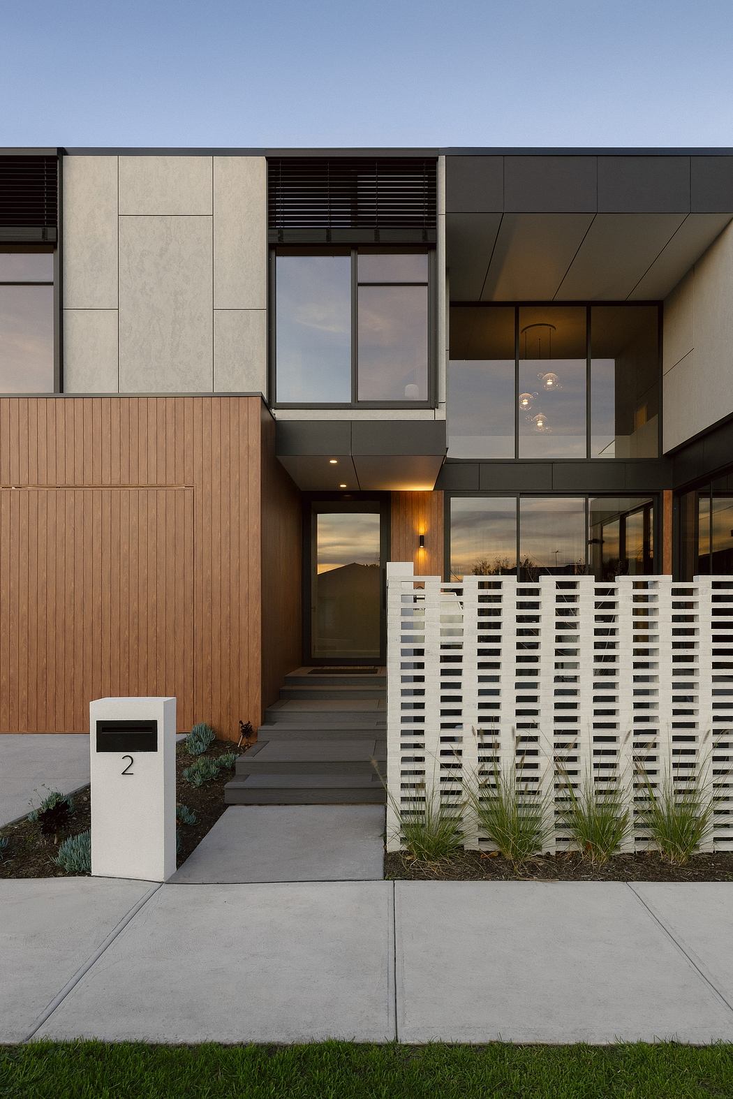 Modern exterior with concrete, wood, and glass elements; landscaping and lighting.
