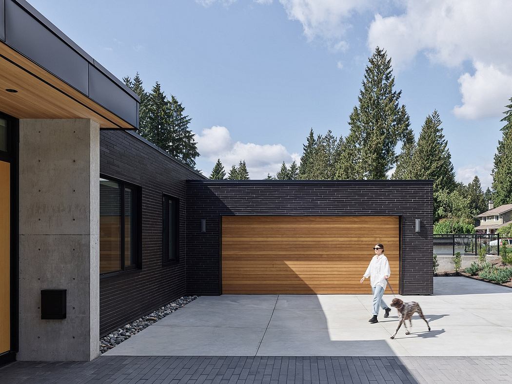 A modern home with a mix of wood, concrete, and dark brick accents, surrounded by lush evergreens.