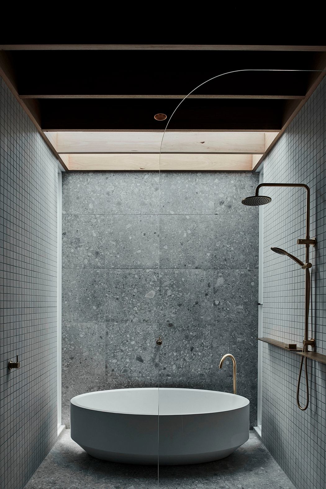 Minimalist bathroom with grey stone tiles, free-standing tub, and modern shower fixture.