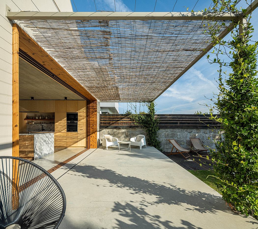 Outdoor patio with woven bamboo roof, concrete floors, and integrated kitchen. Lush greenery and modern furniture.