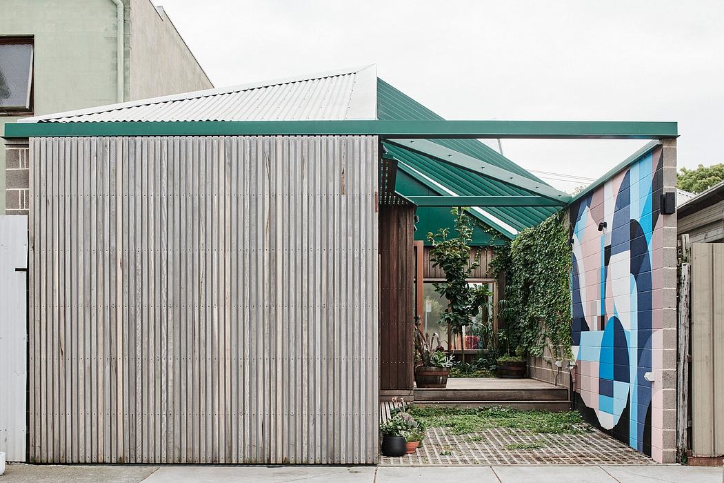 A modern, mixed-use building with a corrugated metal exterior, vibrant green awning, and lush greenery.