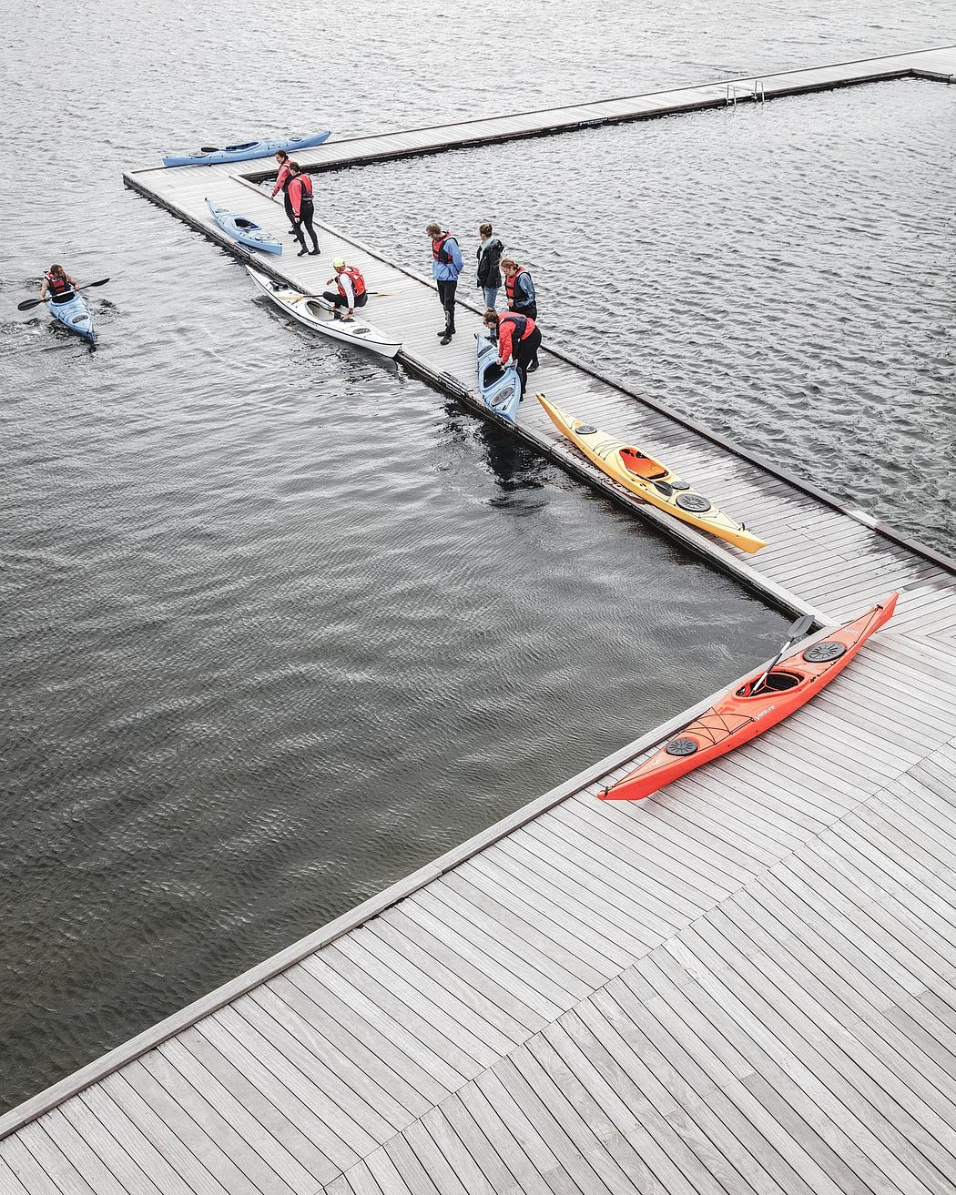 Wooden dock with kayaks and people, surrounded by calm water and overcast sky.
