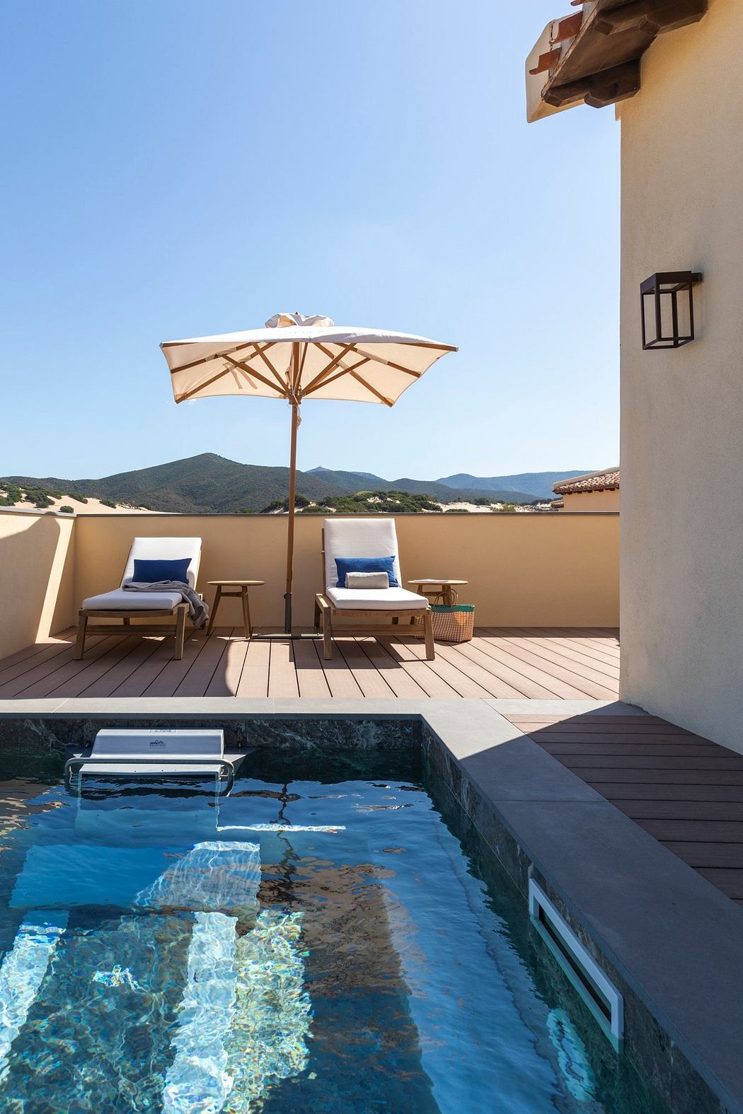 Sun-drenched patio with plush loungers, wooden umbrella, and picturesque mountains.