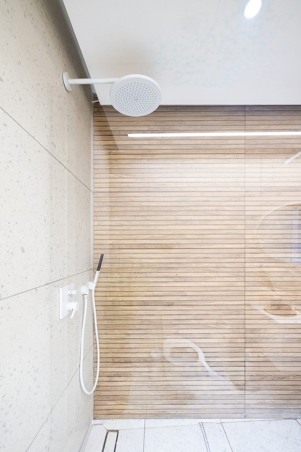 A modern bathroom with a white shower head and wooden paneled wall providing a minimalist aesthetic.
