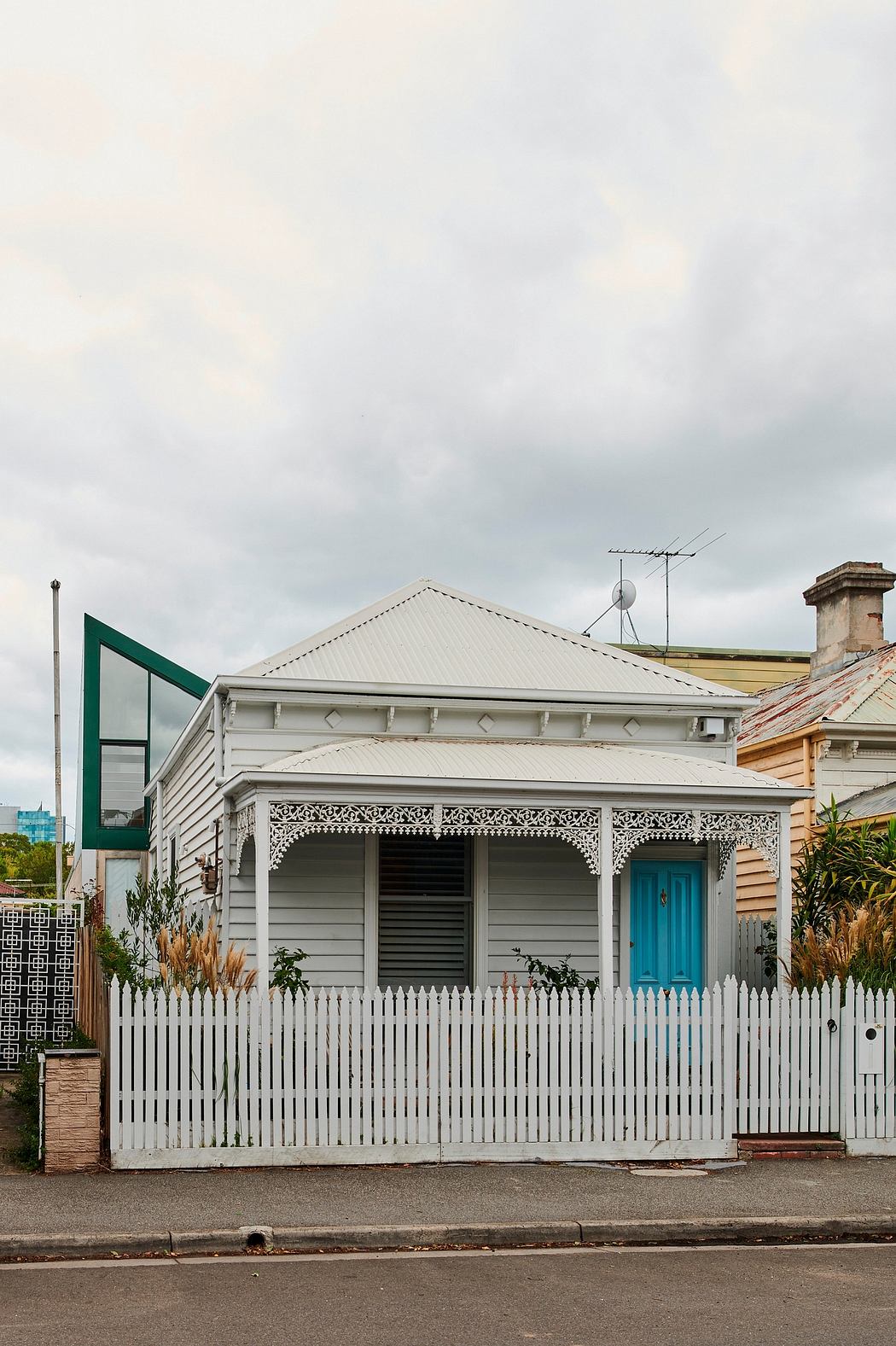 Weathered wooden home with ornate porch, white picket fence, and turquoise door.