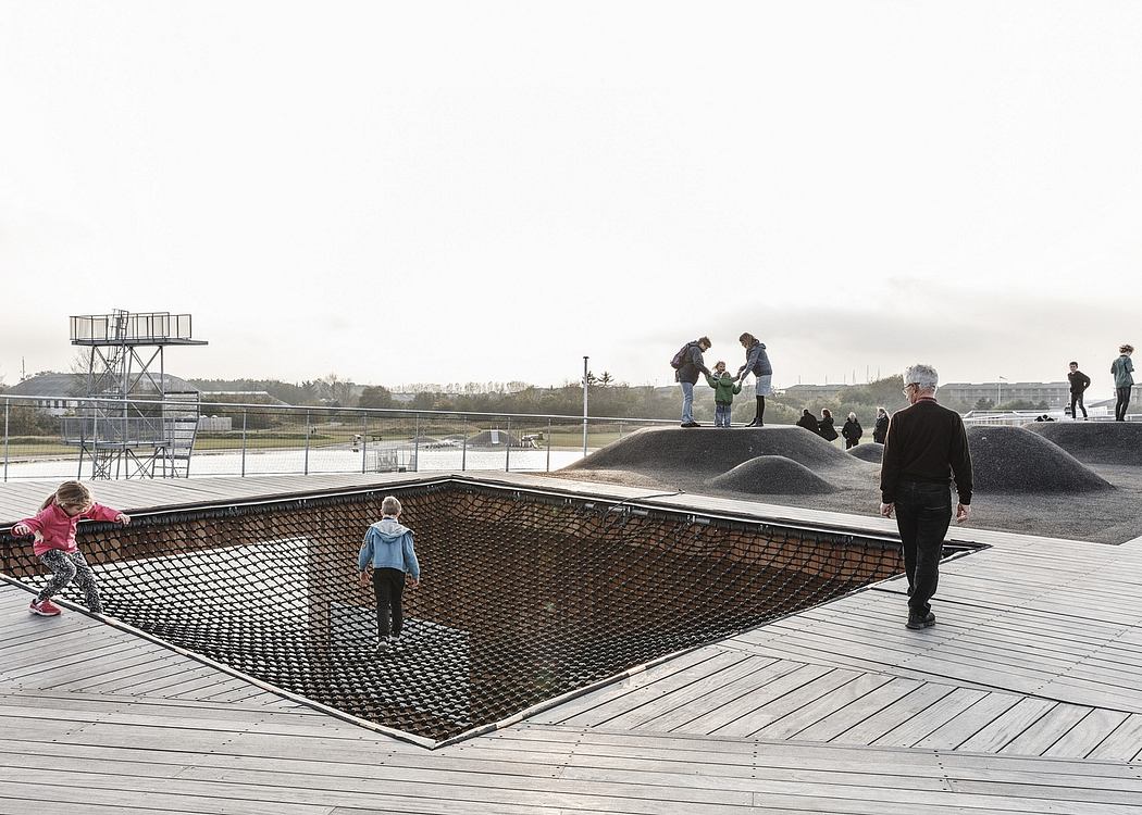 A modern and interactive skate park with trampoline-style netting, ramps, and platform.