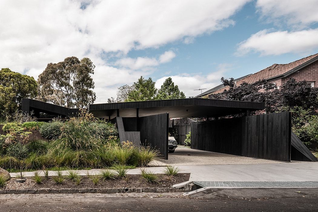 A modern, dark-colored wooden structure with a curved roof, surrounded by lush greenery.