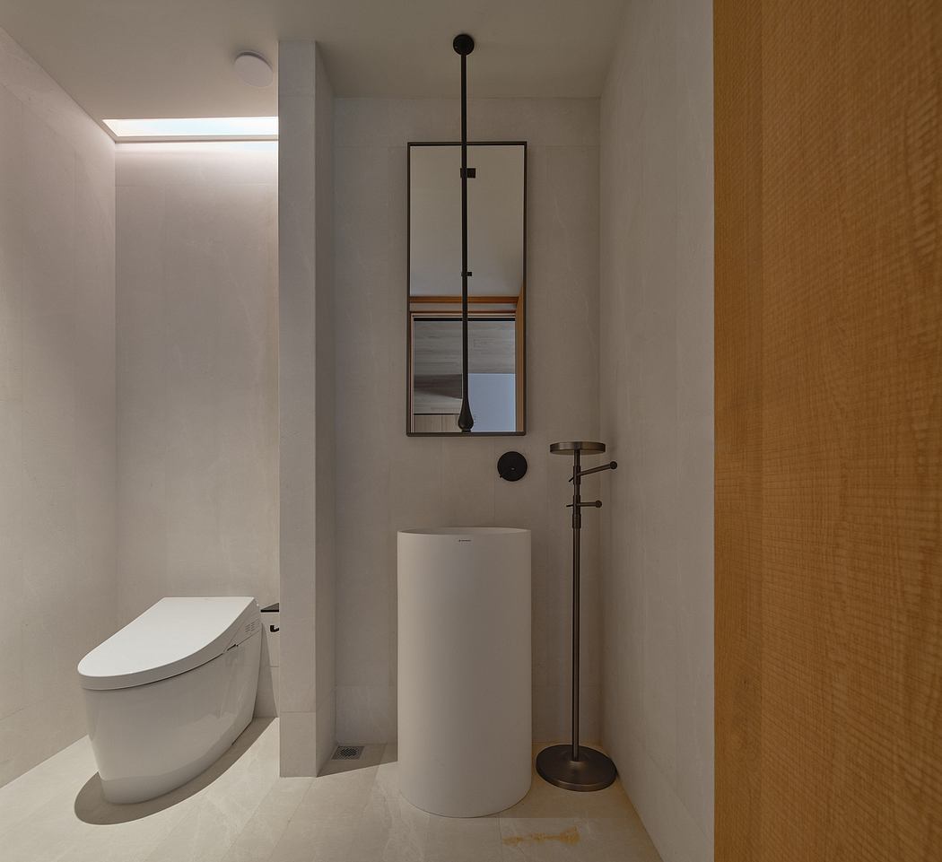 Minimalist bathroom with sleek white toilet, wall-mounted mirror, and modern lighting fixture.