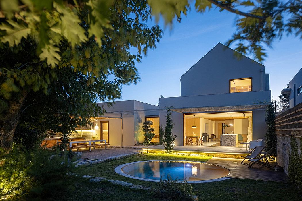 A modern, minimalist home with a circular pool and lush landscaping at night.