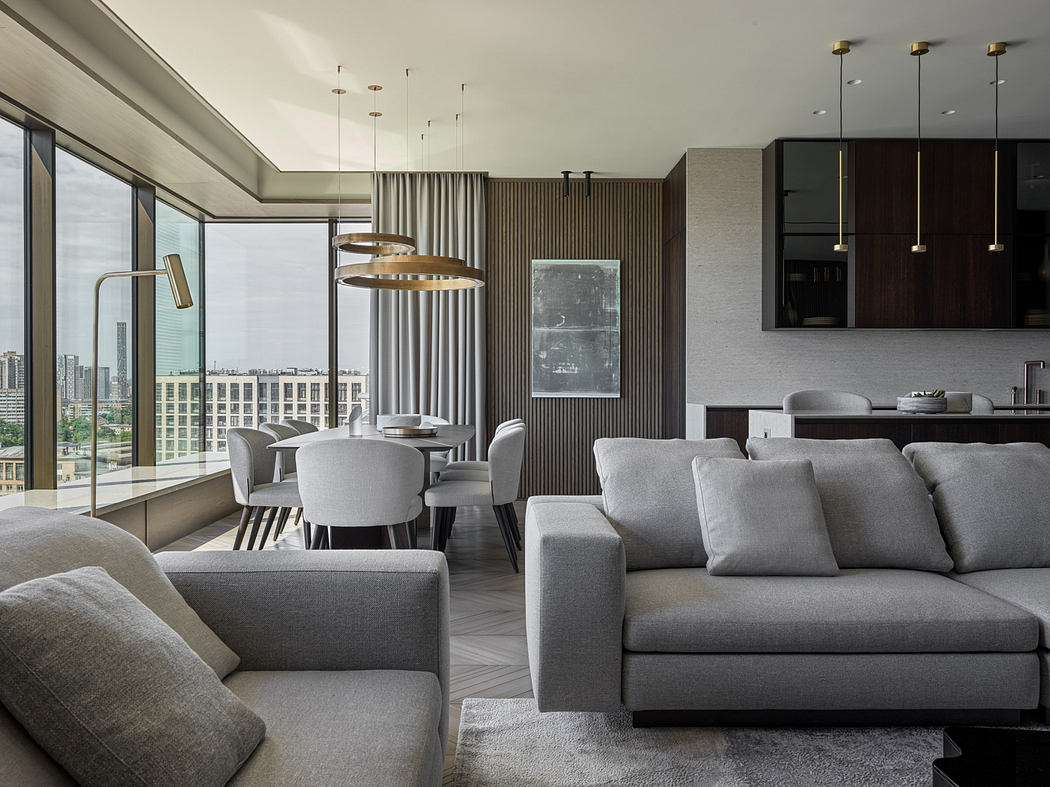 The image depicts a modern and spacious living room with a minimalist, contemporary design. The room features large windows, neutral-colored furniture, and sleek lighting fixtures.