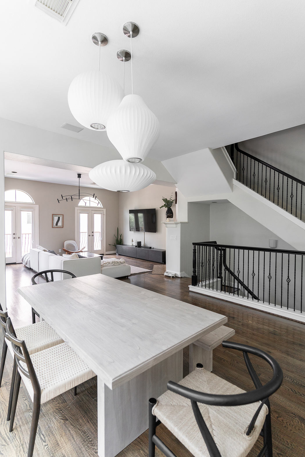 Minimalist open-concept living area with white pendant lights, wooden dining table, and stairs.