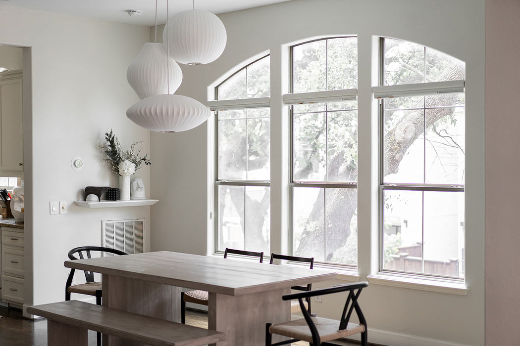 Spacious modern dining area with arched windows, statement light fixtures, and wood furnishings.