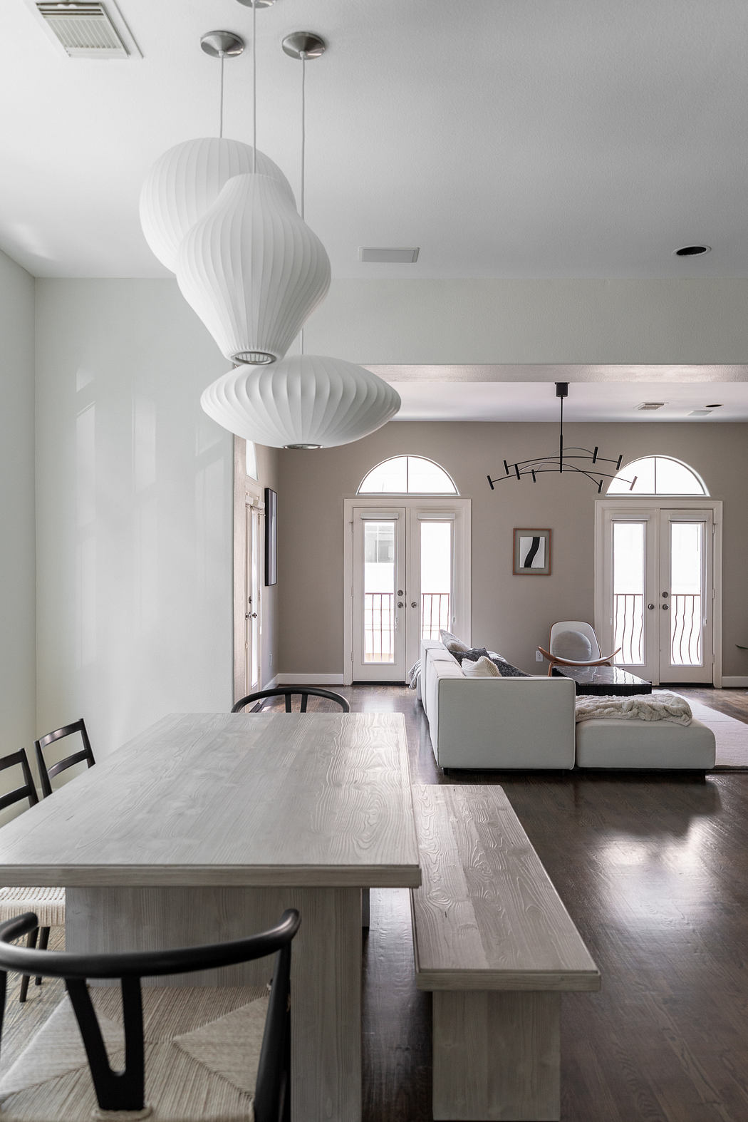 Elegant open-plan living space with white sphere lighting fixtures, wooden table, and arched windows.