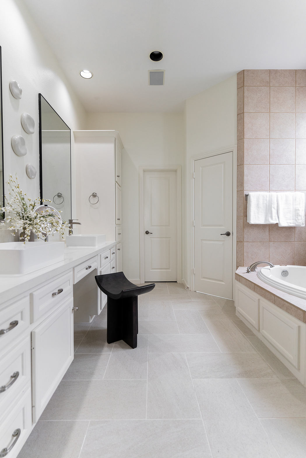 A spacious, modern bathroom with clean white tiled floors and a vanity with dual mirrors.