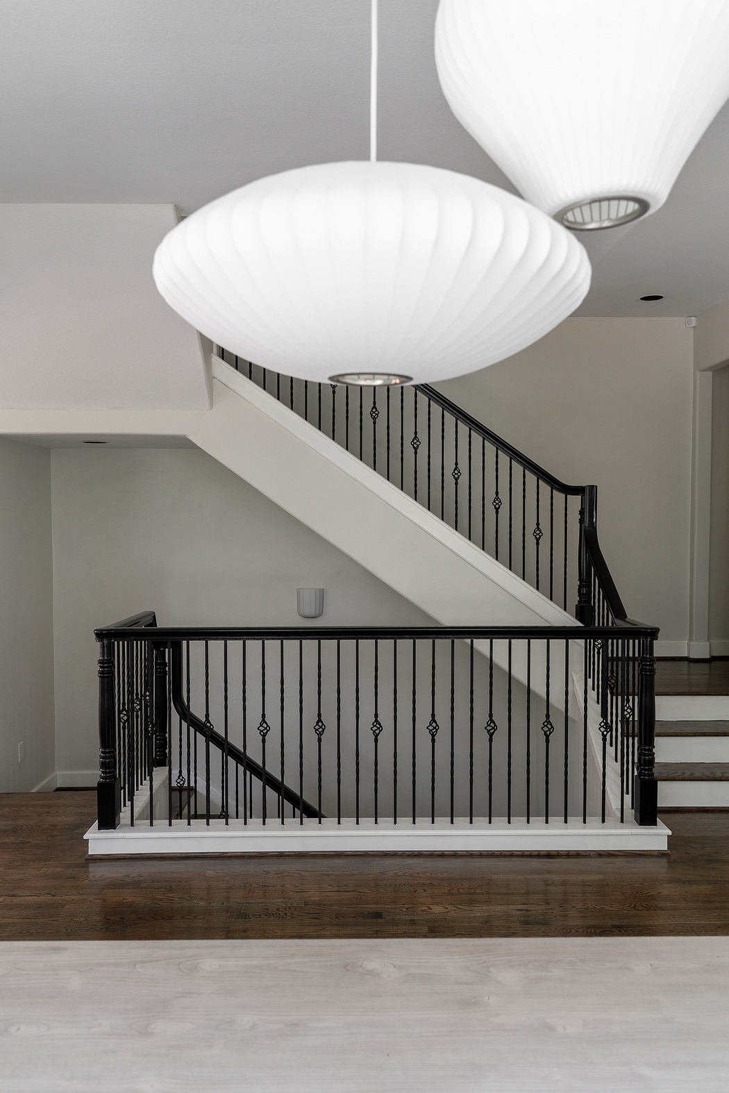 Elegant staircase with ornate metal railing and pendant lighting in modern interior.