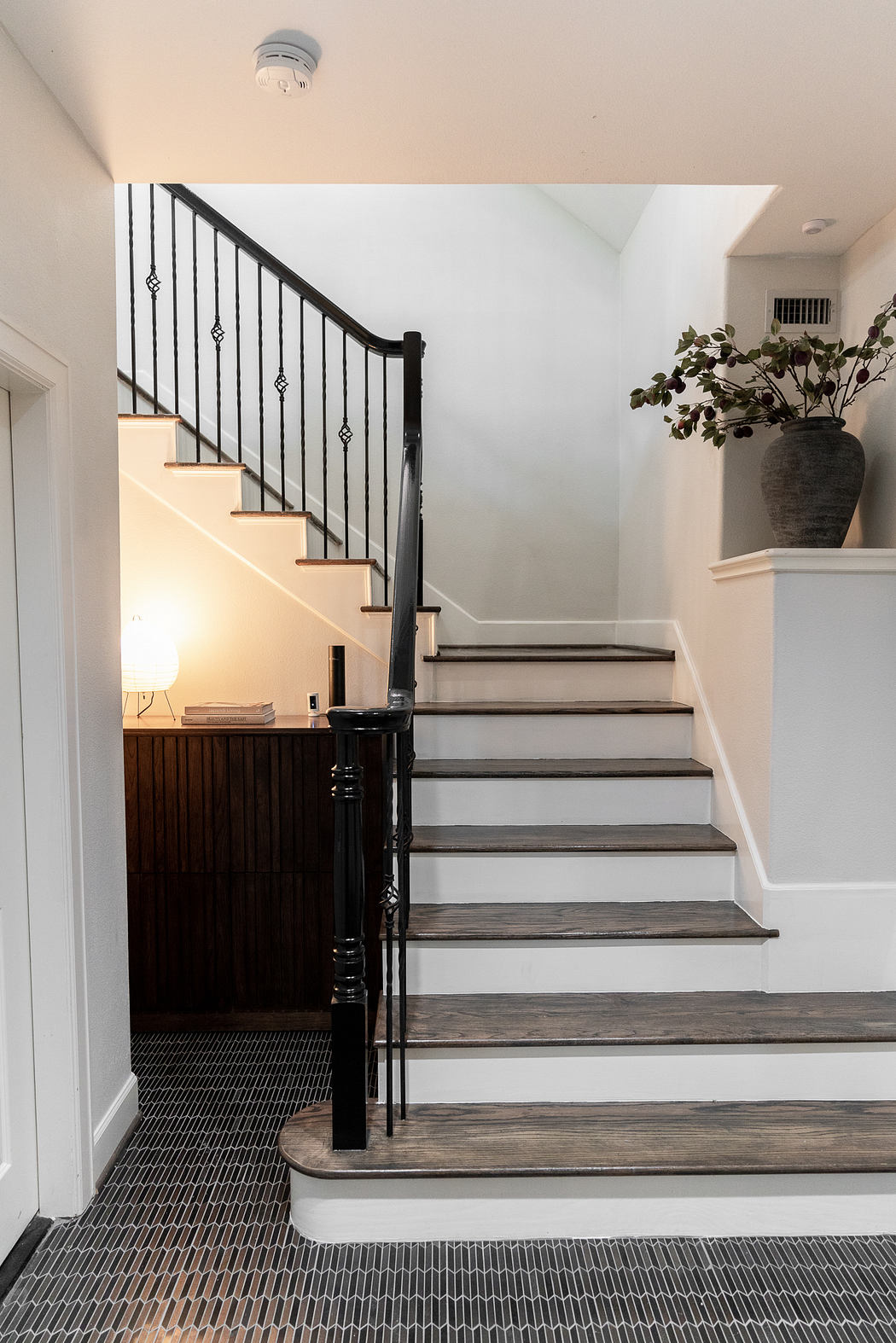 Well-designed staircase with dark wood treads and wrought-iron railings, complemented by a potted plant and minimalist decor.