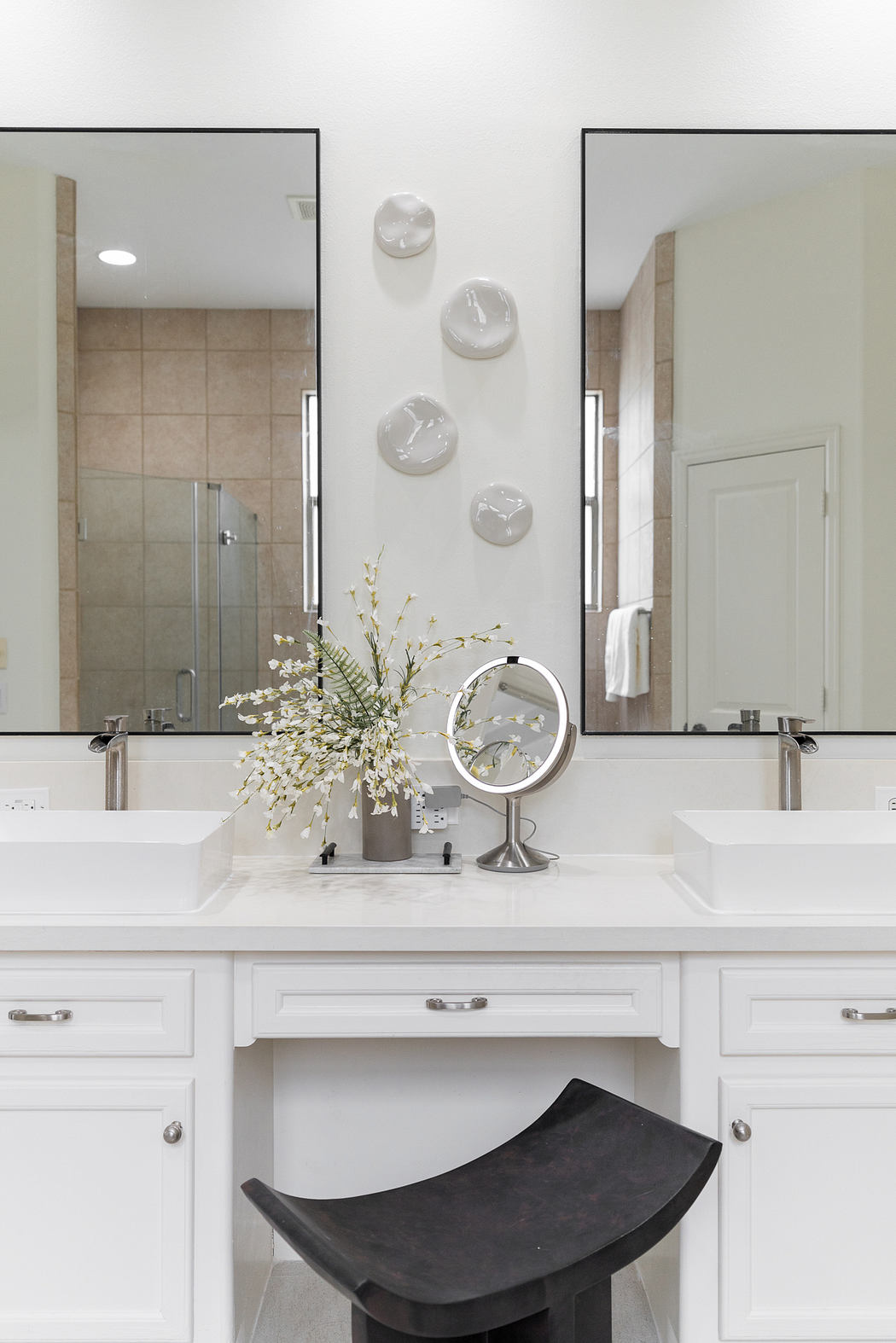 Sleek, white double vanity with mirrors, decorative wall accents, and a black stool - a modern bathroom design.
