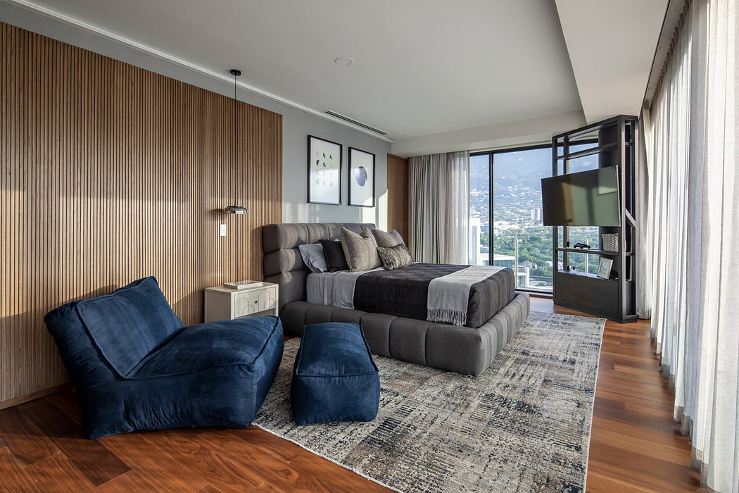Spacious modern bedroom with wood-paneled walls, plush seating, and panoramic city view.