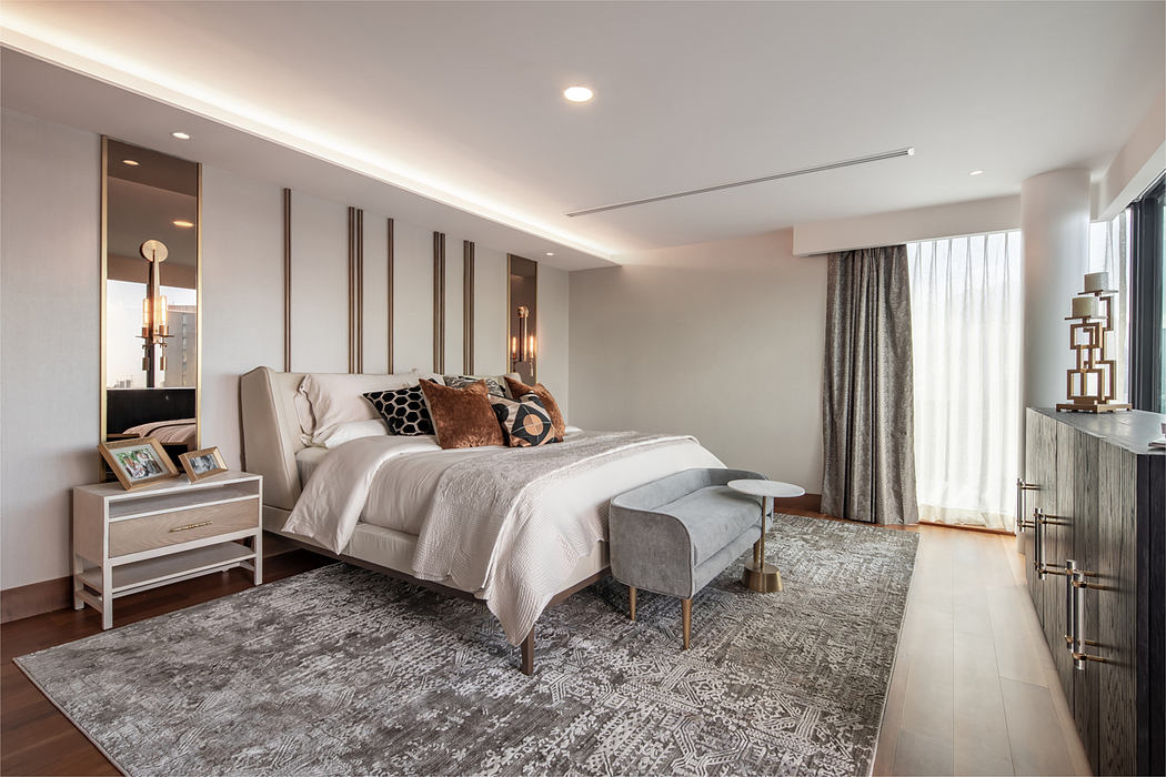 Spacious bedroom with modern decor, warm lighting, and intricate rug pattern.