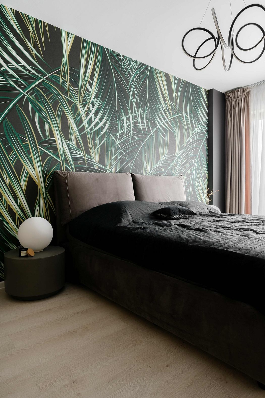 A modern bedroom with a large tropical leaf wall mural, gray bedding, and contemporary lighting.