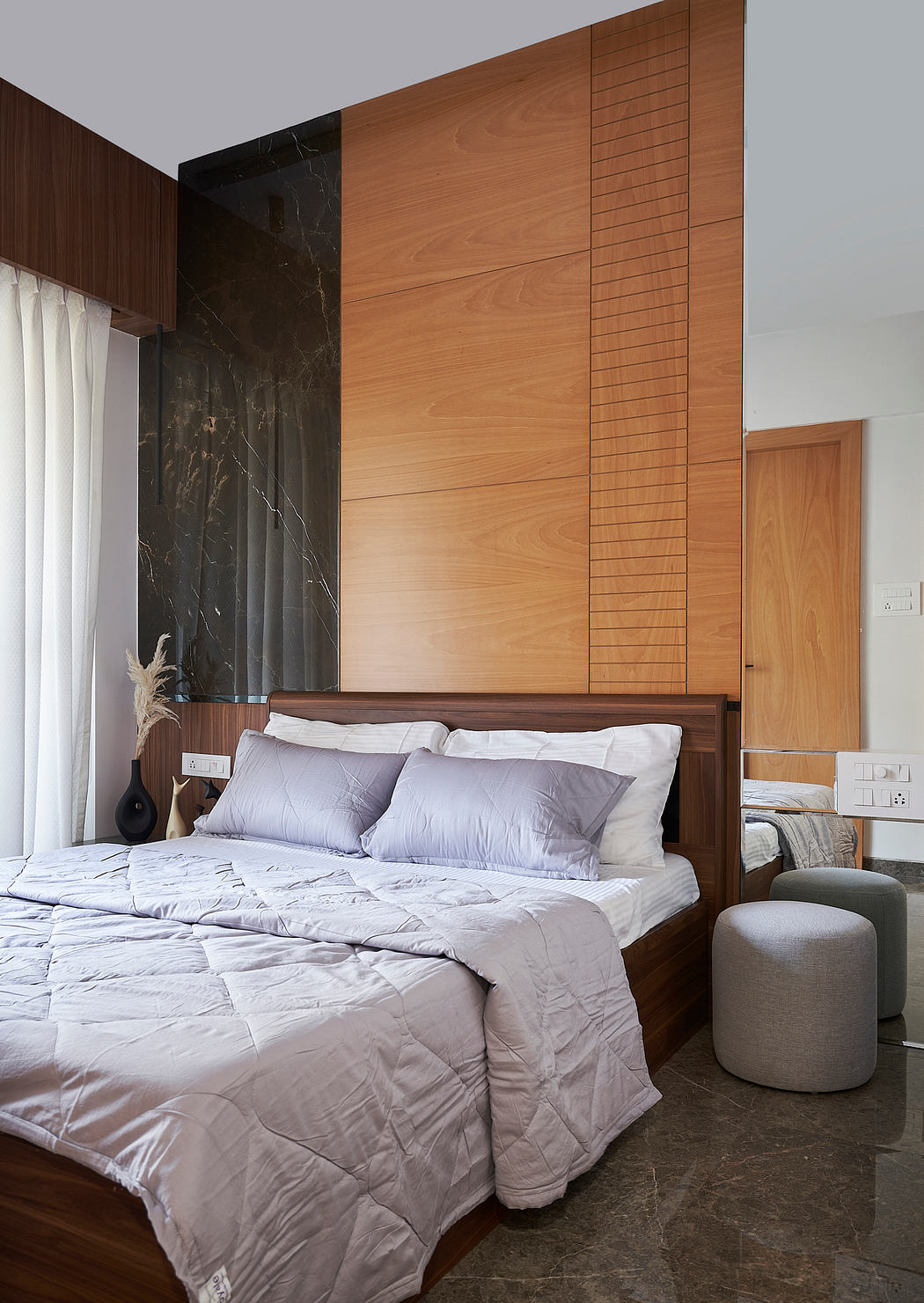 Large bed in minimalist bedroom with marble accent wall and wood paneling.