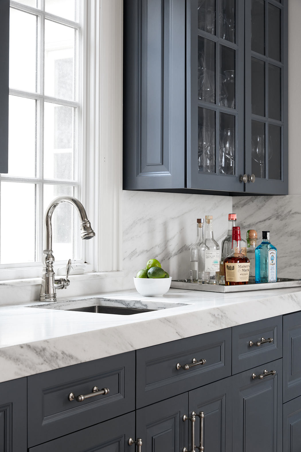 Dark grey cabinetry, marble countertops, and stainless steel fixtures in a modern kitchen.