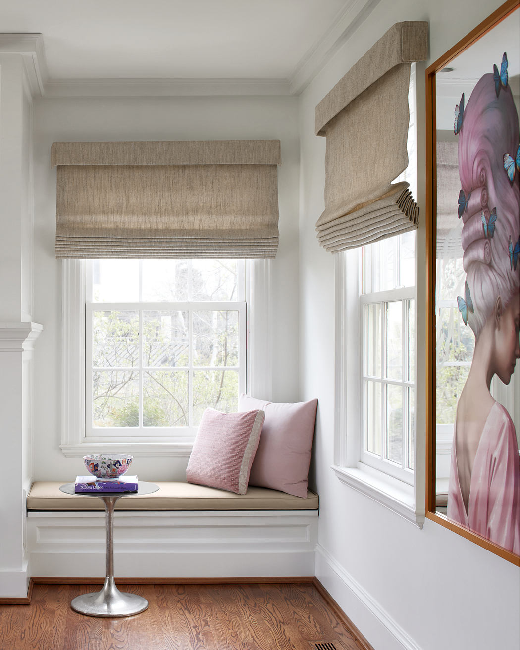 A cozy window nook with custom built-in seating, linen Roman shades, and a large artwork.