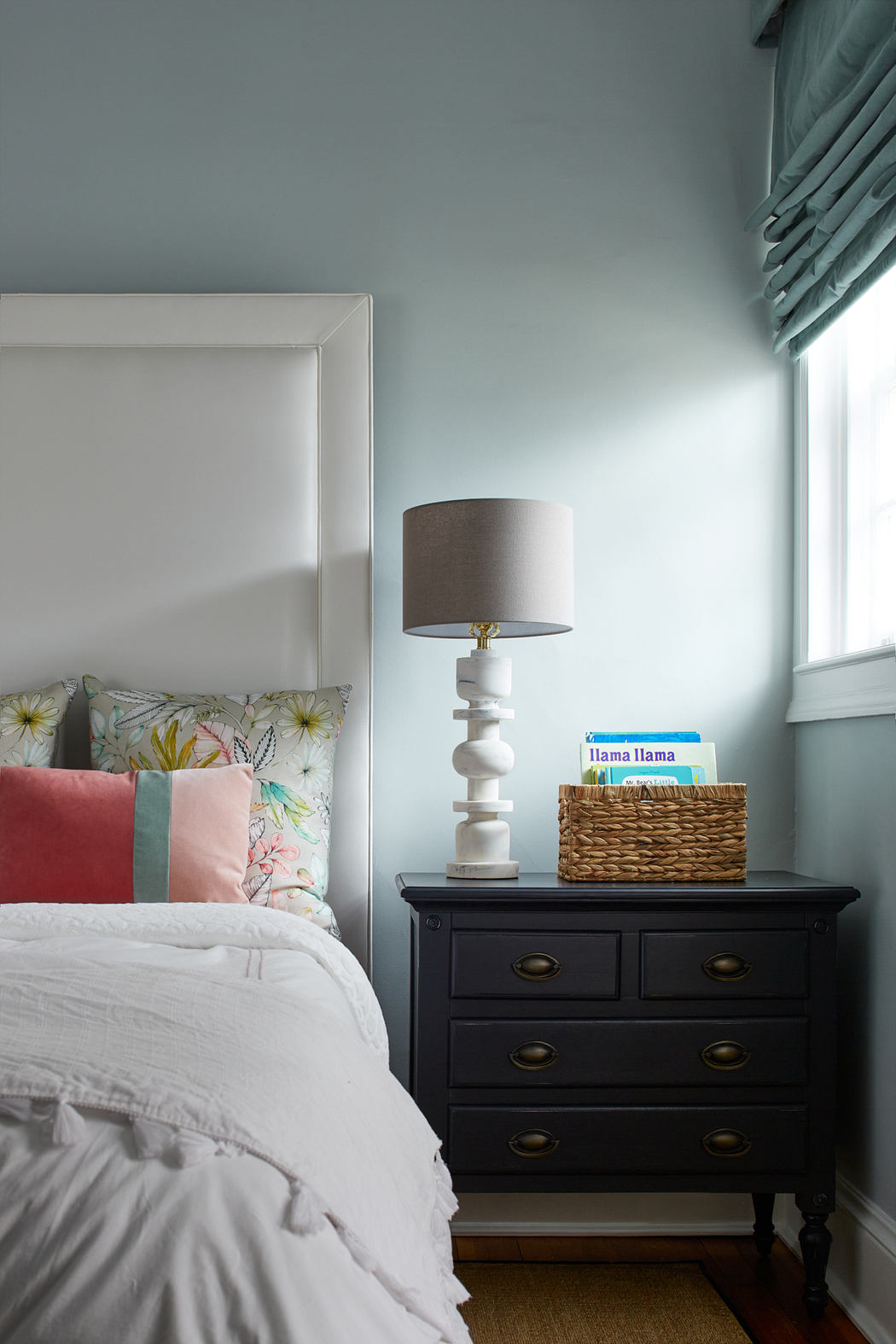 Cozy bedroom with a white-framed bed, a black wooden dresser, and a table lamp.