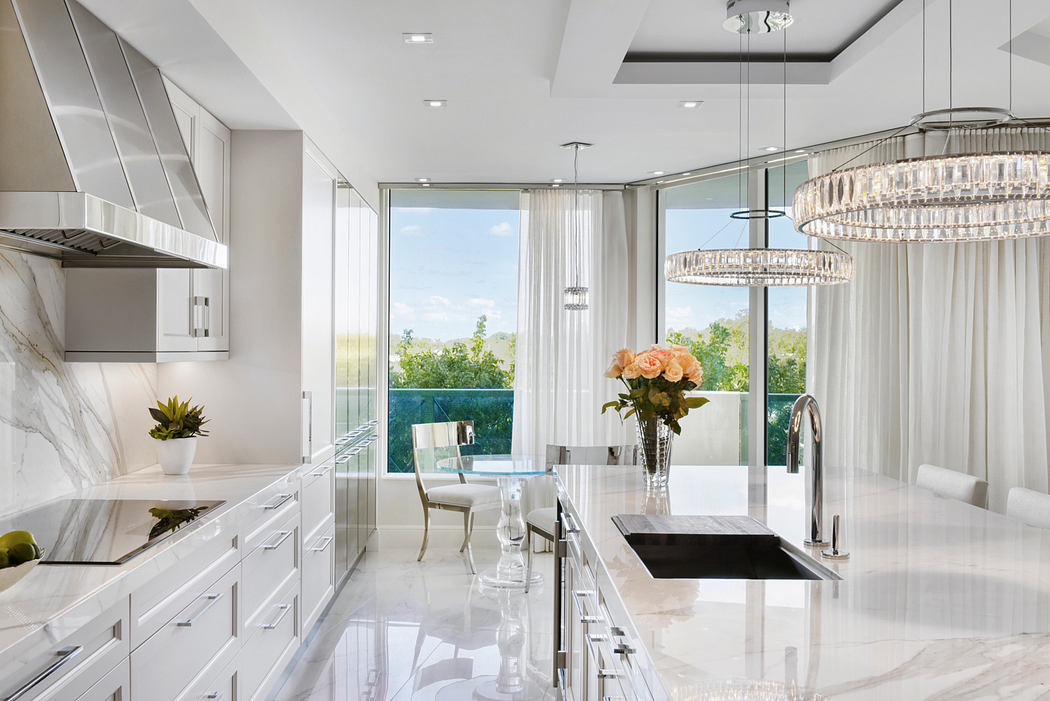 Luxurious, modern kitchen with sleek marble countertops, chandelier, and floor-to-ceiling windows.