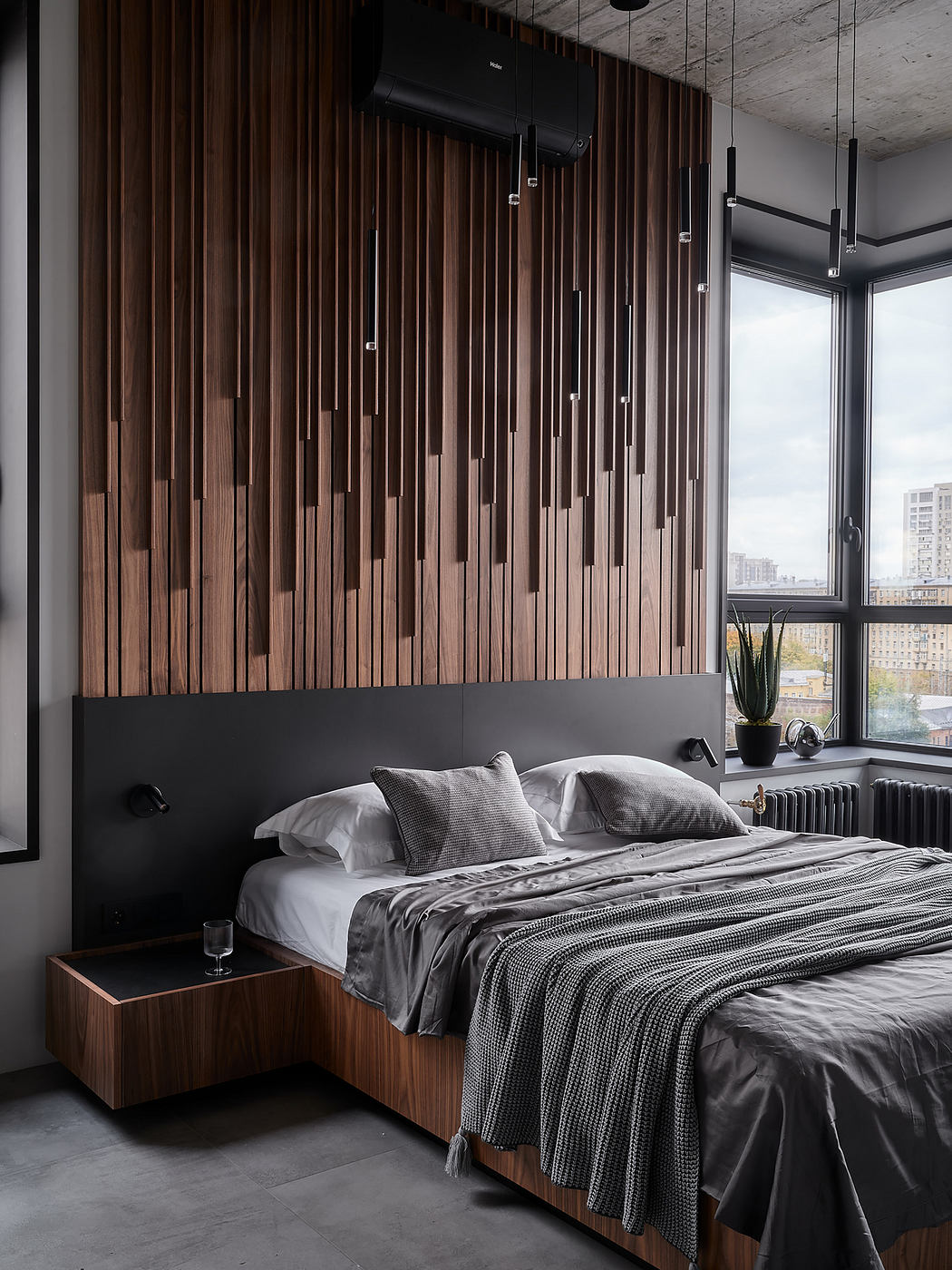 Modern bedroom with striking wooden paneled wall, minimalist furnishings, and city skyline view.