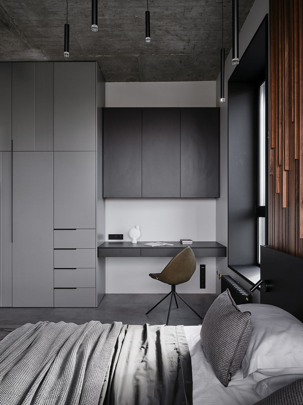 Modern minimalist bedroom with concrete ceiling, black built-in cabinets, and a desk area.