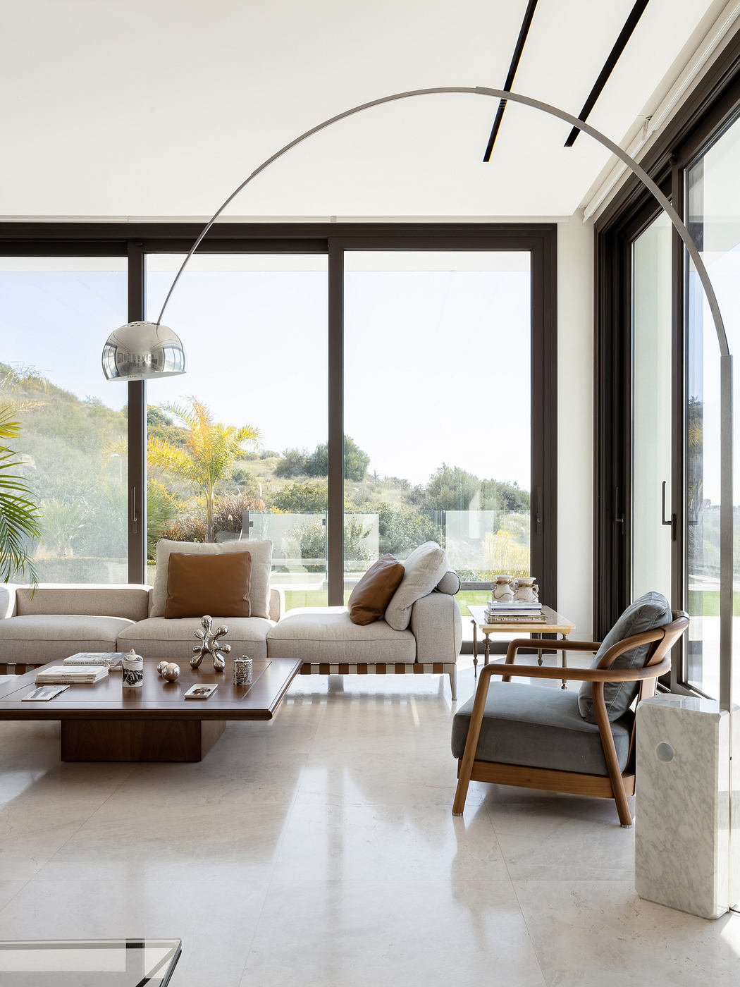 Minimalist living room with sleek glass windows, curved lighting fixture, and natural materials.