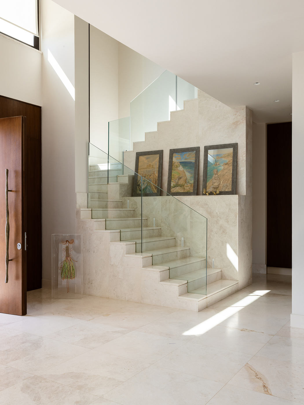 Sleek, modern staircase with glass balustrade and framed artwork on the walls.